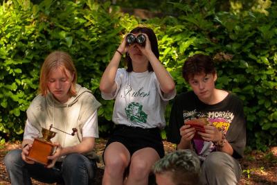 meisjes zitten buiten en een meisje kijkt door een verrekijker tijdens theater kamp in west-vlaanderen